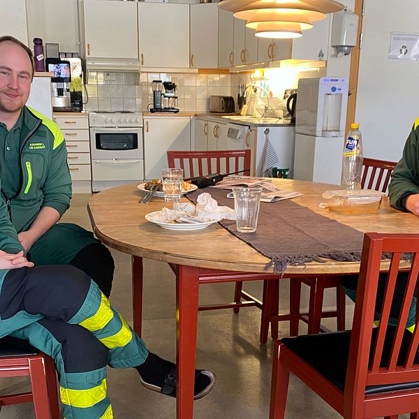 Ambulanspersonal vid lunchbord som tittar in i kameran