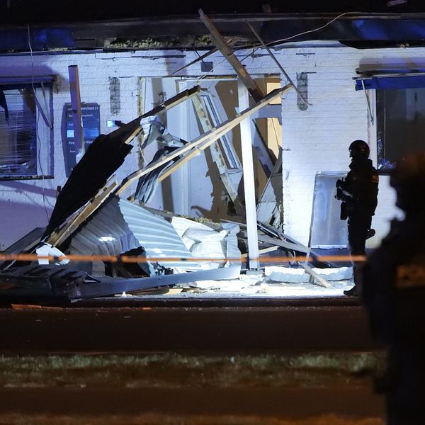 Entrén till en byggnad skadad av en explosion på Råå i Helsingborg. Beväpnad polis bevakar.