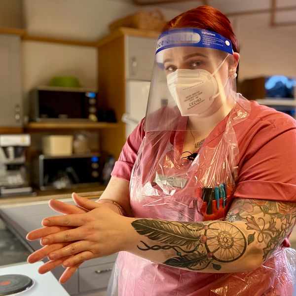 Emma Fjellner står i ett kök i full skyddsutrustning och smörjer in händerna med alkogel.