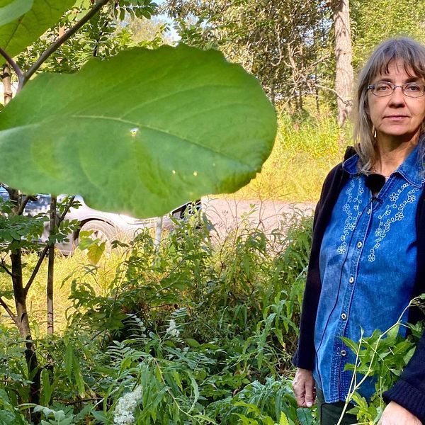Lena Bondestad – en medelålders kvinna – står bland grön växtlighet vid sidan av en grusväg