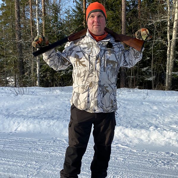 Jägaren Anders Gravsjö i Rättvik står mitt i bild med geväret vilande över axlarna. I bakgrunden står träd och marken är snöig.