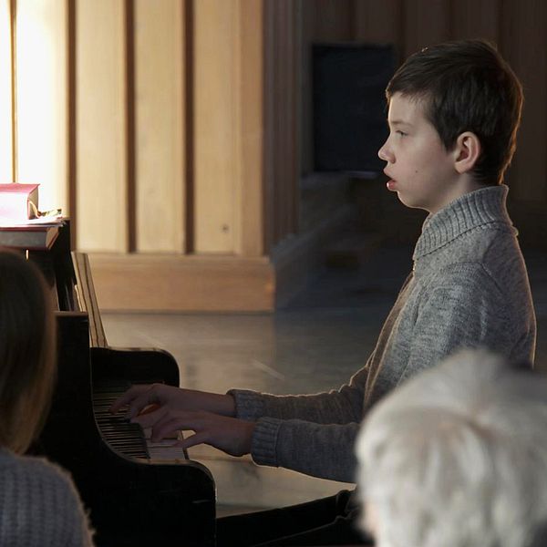 En pojke sitter vid ett piano och spelar framför en publik.