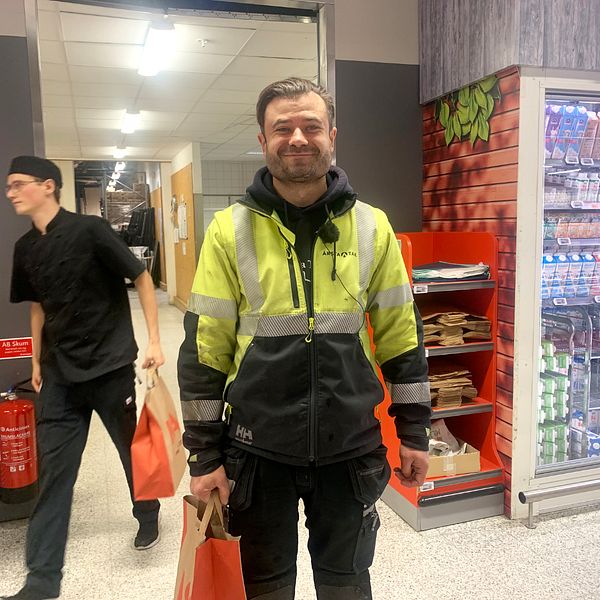 Pawel Trzecinski, iklädd nyongula arbetskläder står framför ingången till lagret i en matbutik. I ena handen håller han en matkasse.