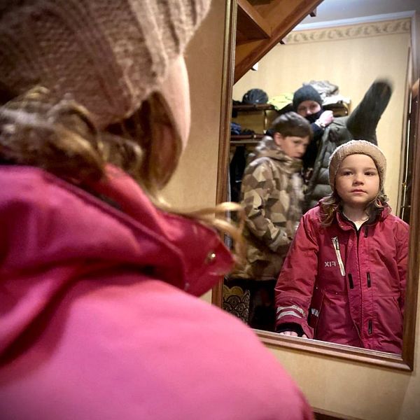 En familj under morgonen på väg ut, medan föräldern och ett barn tar på sig kläderna står dottern och tittar sig i hallspegeln.