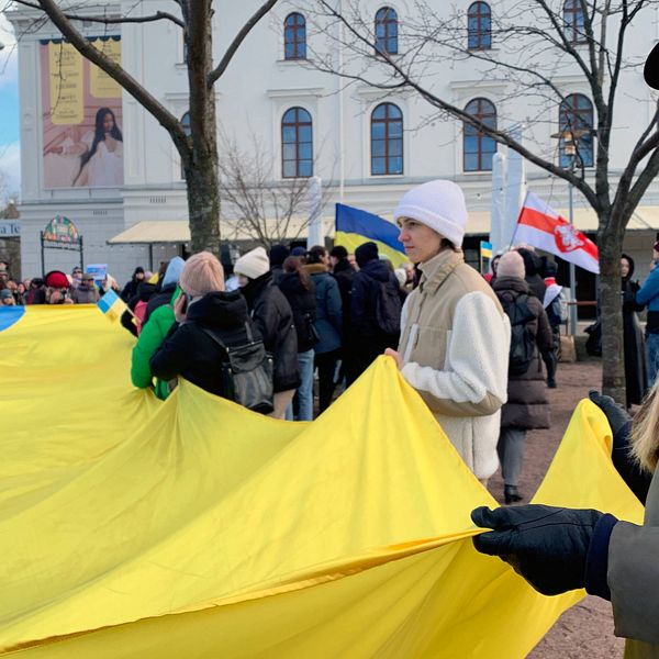 Människor utanför Stora teatern i Göteborg håller i en stor ukrainsk flagga. En tjej tittar in i kameran.