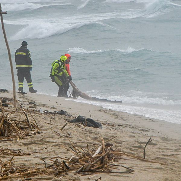 En person dras upp på stranden av italiensk räddningstjänst. På havet går det stora vågor.