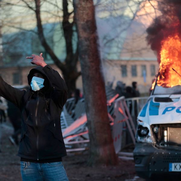 En man i maskering tar en selfie på sig själv och en brinnande polisbil i bakgrunden under påskupploppen i Örebro.