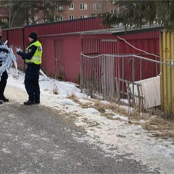 Två polisen står och samtalar på en liten grusväg. Den ene håller avspärrningsband i handen.