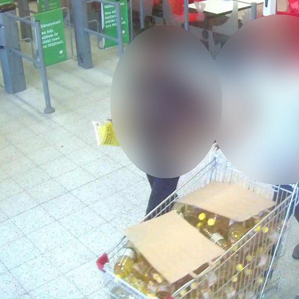 Blurrad bild inifrån en matvarubutik. Två personer går med en kundvagn full med rapsolja. Båda personerna är blurrade.