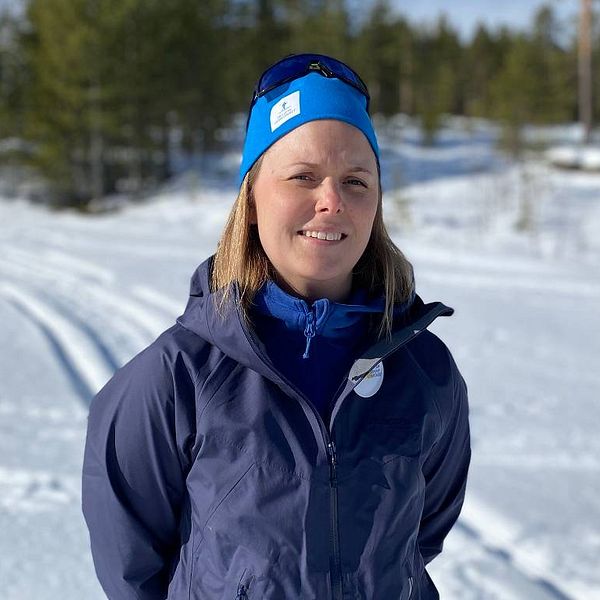 Blond kvinna i blå jacka och blå mössa, står i Hedebacken i Hede, Härjedalen.