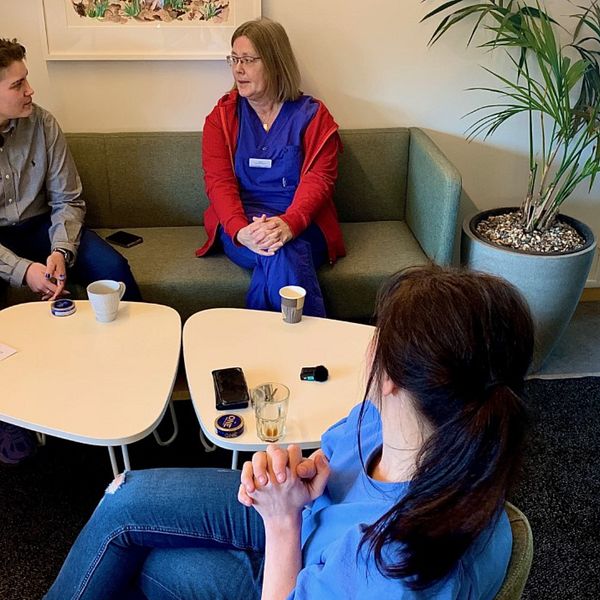 En ung kille i grå skjorta sitter och pratar med en vårdpersonal som bär regionens blå arbetskläder. Mittemot dem sitter Kajsa Sjöberg i blå tröja hon är vårdenhetschef.