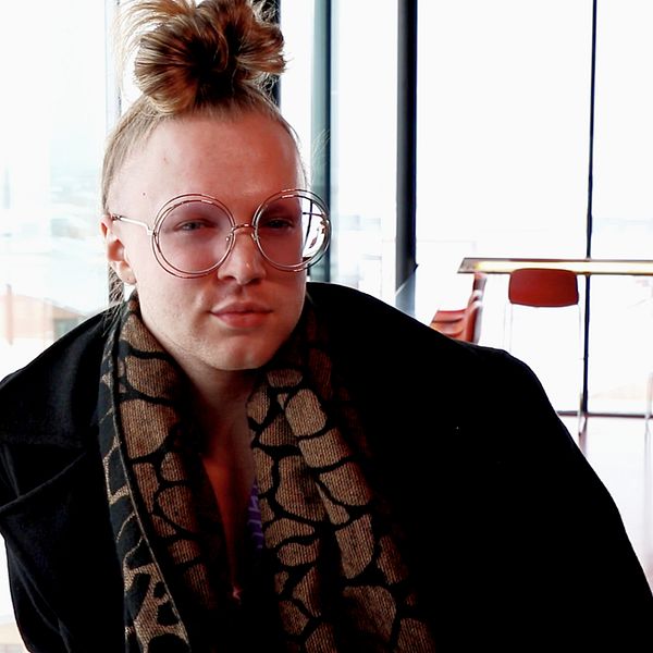 En ung man med håret knutet ovanpå huvudet sitter framför en glasvägg.