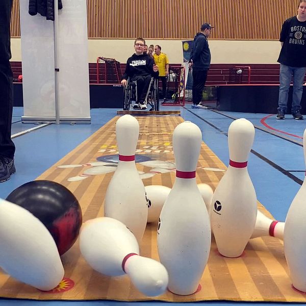 Pojke i rullstol har kastat ett bowlingklot som fäller flera käglor.