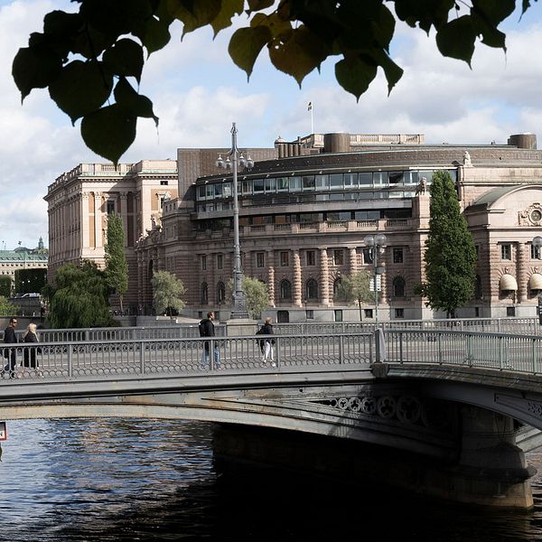 Riksdagshuset i septembersolen. Några löv syns i förgrunden.