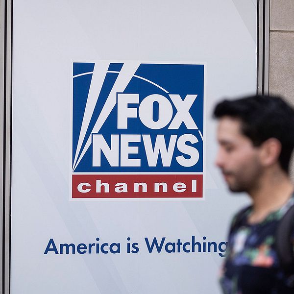En man går förbi en Fox News-logotyp på en husbyggnad.
