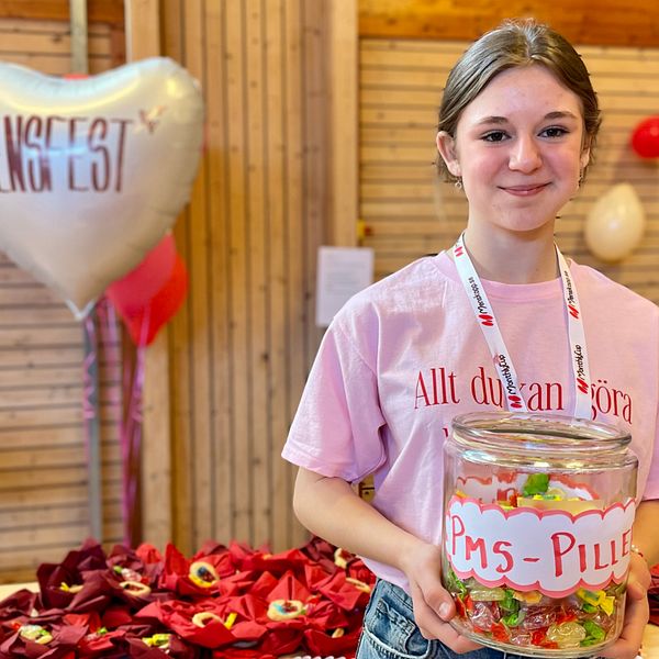 Otilia Clifford är en av initiativtagarna till Rönnbyskolans mensfest. Bakom henne på bordet ligger origamisnippor med snippkakor. Runt omkring i salen är det pyntat med ballonger. En ballong som är hjärtformat där står texten mensfest.