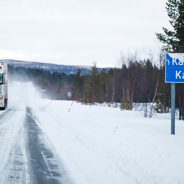 lastbil på en snåig väg vid infarten till Karasjok, vägskylt med ortnamnet till höger