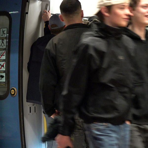 Bild på pendeltåg på station och resenärer som går in i tåget, dörren öppen.