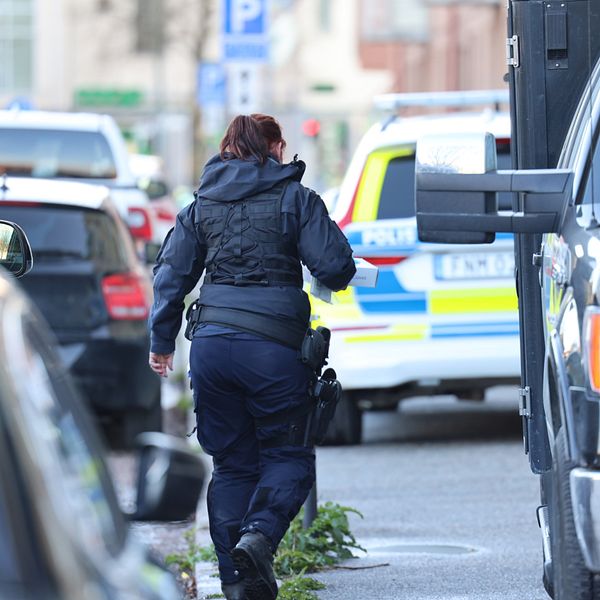 En kvinna i poliskläder går mellan bilar.