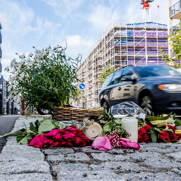 En bild på Långströmsgatan i Göteborg, där en bild passerar bakom flera blommor lagda på kullersten bredvid vägen.