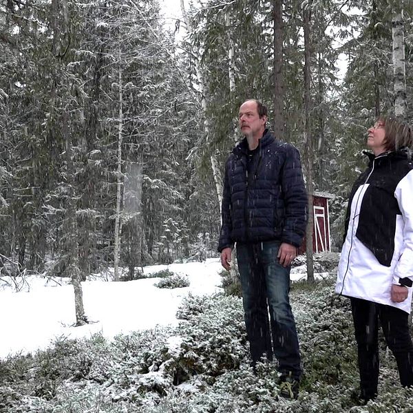 Lena Mikaelsson står tillsammans med sin man ute i skogen i Nästansjö. Hon har ljus page och glasögon. Det snöar i bakgrunden.