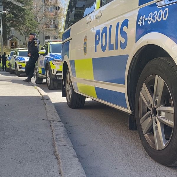 En bild på polisbilar på en gata utanför ett lägenhetshus. Uniformerade poliser står vid några av bilarna.