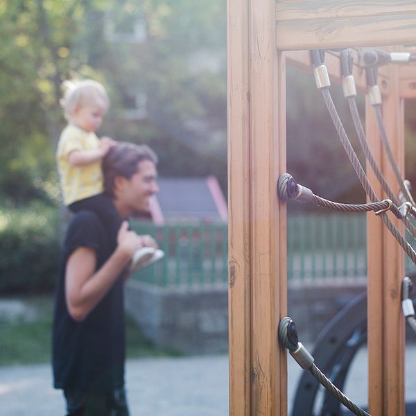 en pappa går med sitt barn på axlarna i en lekpark