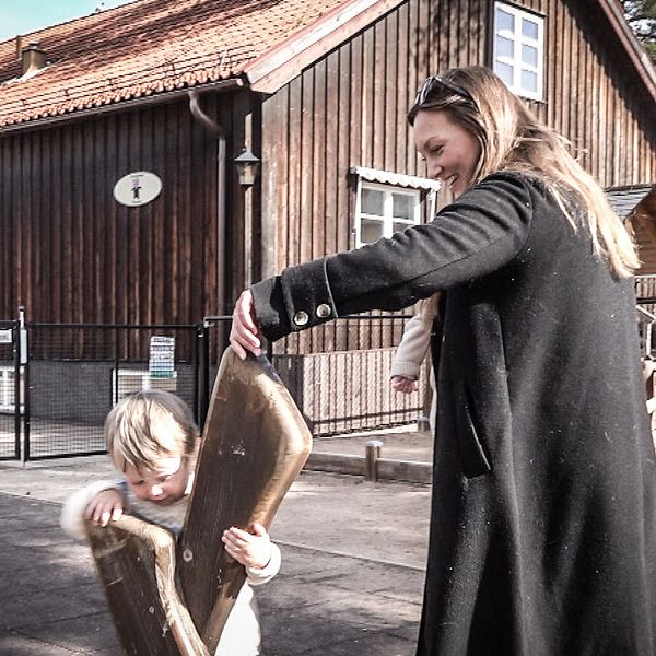 Emma Vikström står på en lekplats i Rättvik och leker med sin son. Hon har långt ljusbrunt hår och svart jacka.