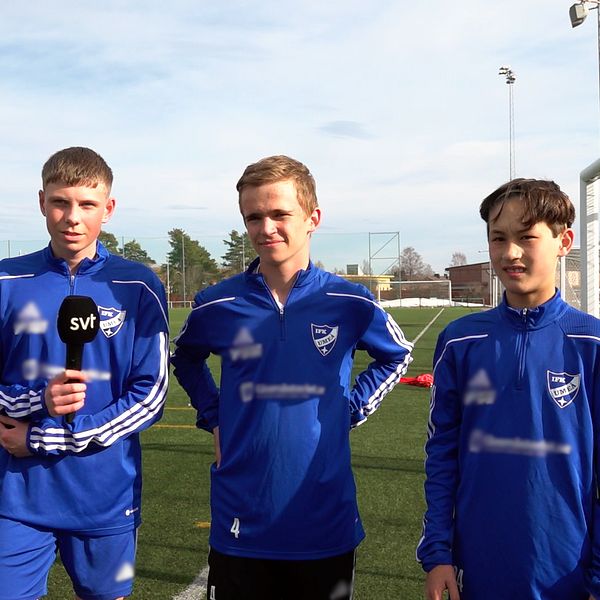 Tre unga killar i blåa fotbollsdräkter på en konstgräsplan