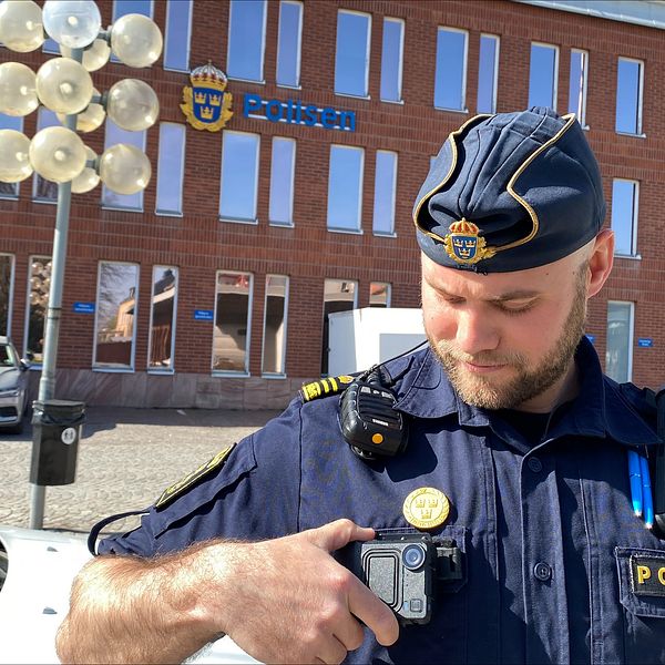 en polis utanför polishuset i Borlänge. Han håller i en kroppskamera som sitter på hans uniform.