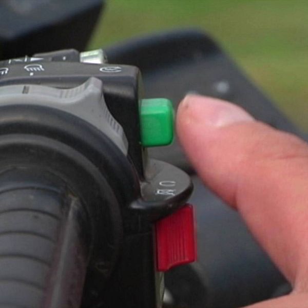 Tät bild på ett styre på en fyrhjuling. En tumme som precis är på väg att trycka på en grön startknapp syns i bilden.