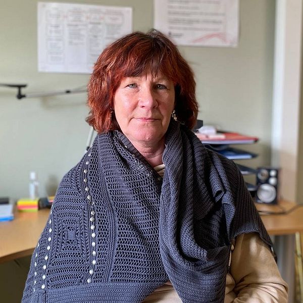 Annika Eriksson, stabschef i vård- och omsorgsförvaltningen, sitter på en stol vid en kontorsplats. Hon har en grå virkad sjal om axlarna och rödbrunt hår.