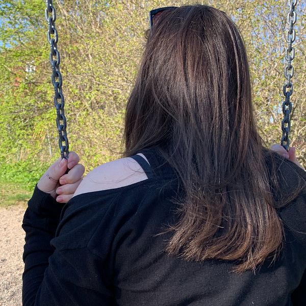 Anonym bild. En tjej i gymnasieålder med brunt hår sitter på en gunga. Bilden är tagen bakifrån så att man inte ser tjejens ansikte.