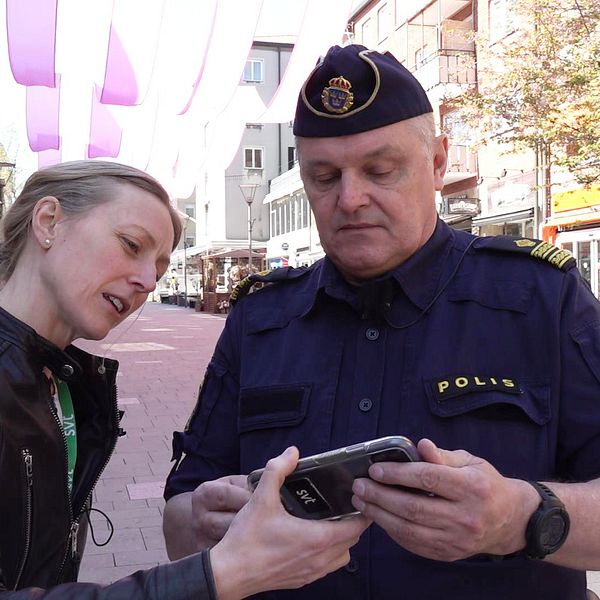 Kvinnlig reporter på SVT visar telefon för manlig polis i centrala Västerås.