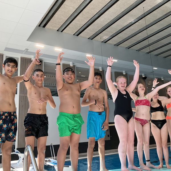 Barn står med händerna över huvudet längs en poolkant.