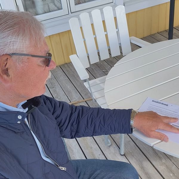 Revisorn sitter utomhus och pekar med handen på ett papper. ”resultaträkning” står det längst upp på pappret. Han har solglasögon och en mörkblå jacka på sig.