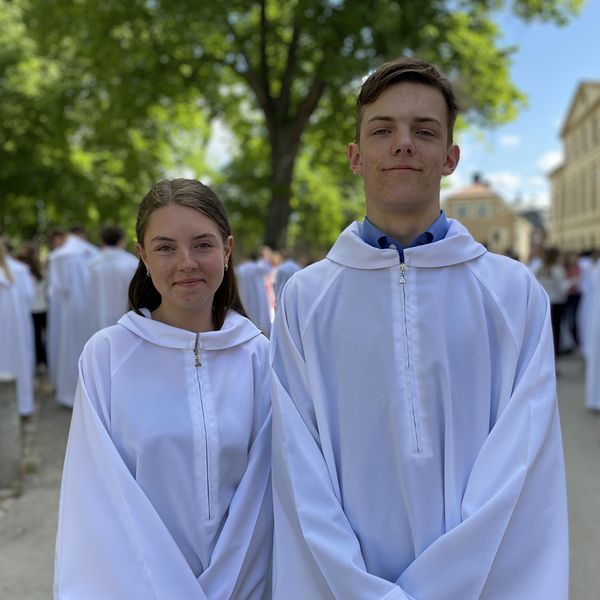 Konfirmanderna Milia Eriksson och Vidar Jonasson Bergstrand står i vita konfirmationskläder utanför Linköpings domkyrka.