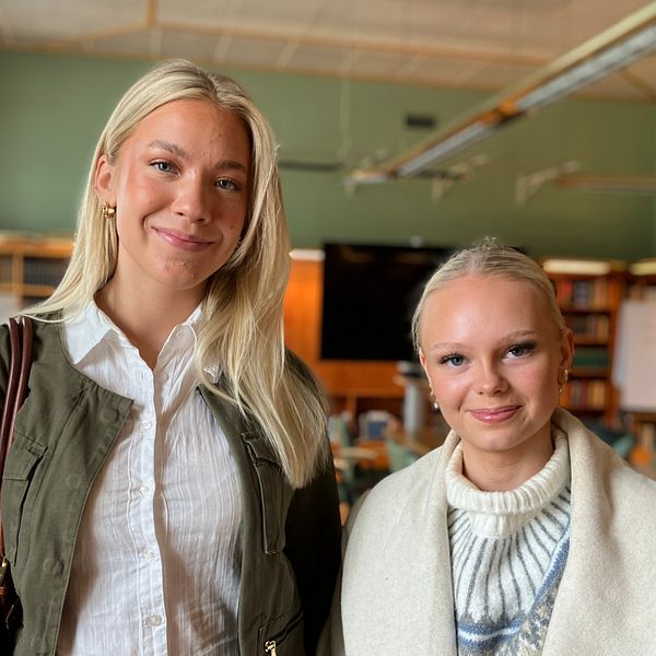 Tyra Nordvall och Liv Sandell Jonsson, två tjejer med blont hår som går på Jämtlandsgymnasium står i en skollokal och tittar in i kameran.