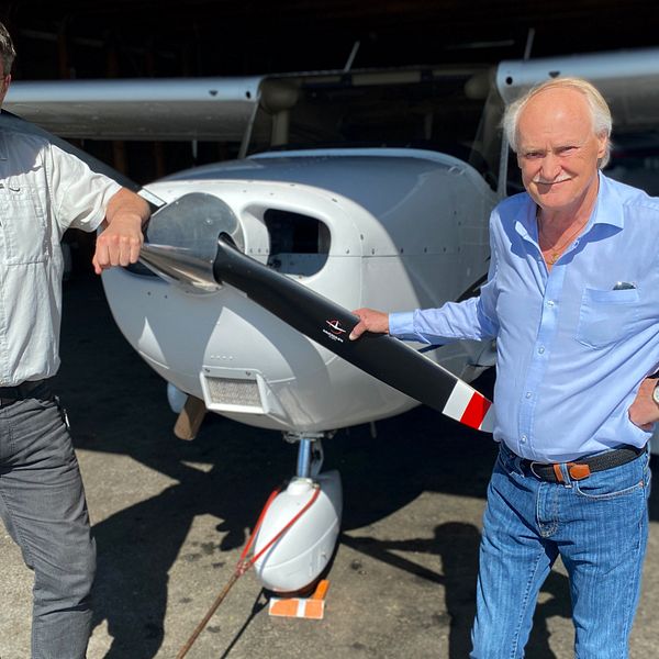 Två män håller i propellern längst fram på ett flygplan.