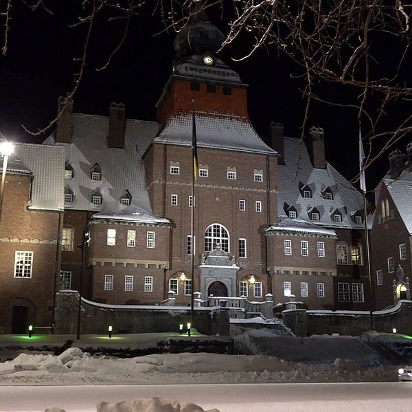 Östersunds rådhus, en stor tegelbyggnad. Det ligger snö på taken och på marken och huset är upplyst av lampor.
