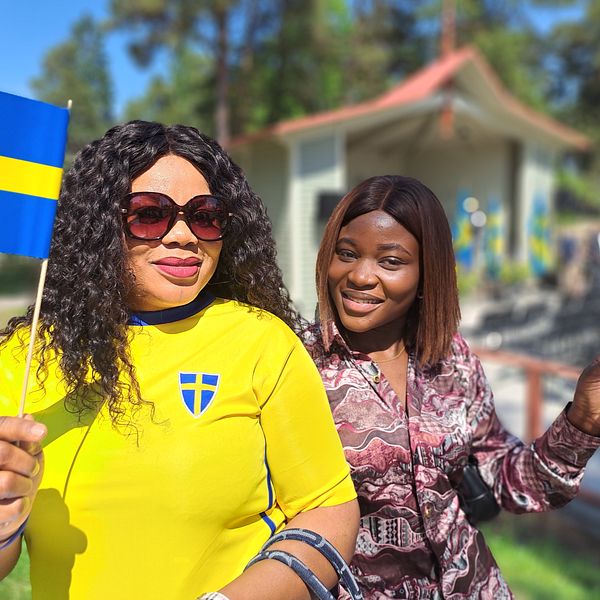 Två kvinnor med svenska flaggor och den till vänster iklädd svensk landslagströja, står framför en scen i Södertälje.