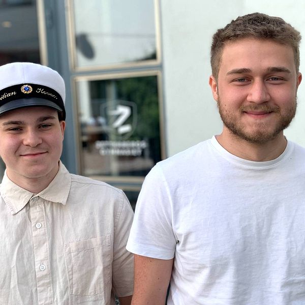 Två unga killar, en med studentmössa, ler mot kameran.