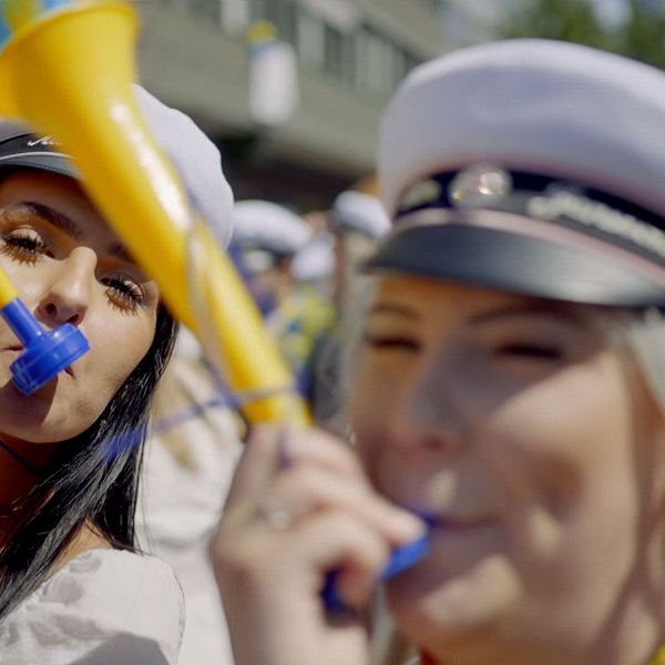 Två unga kvinnor med studentmössor blåser i gula och blå trumpeter i Västerås.