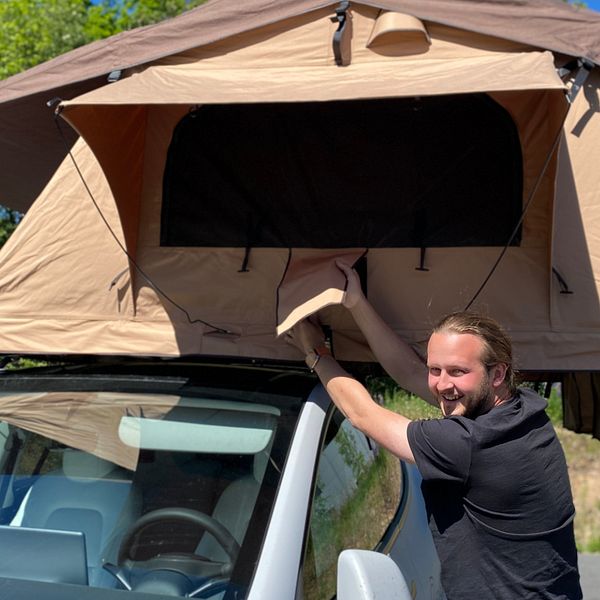 En man står framför en bil som har ett tält på taket.