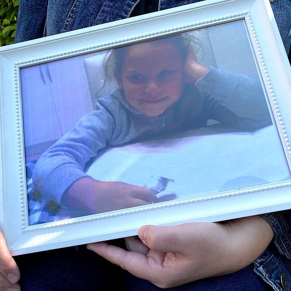 Ett inramat fotografi på Sarah, en sjuårig flicka, som hennes mamma håller upp.