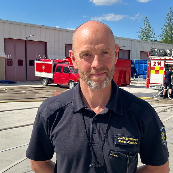 Henrik Jönsson, olycksutredare på räddningstjänsten, en man med kort skägg står framför några brandbilar vid brandstationen i Östersund.