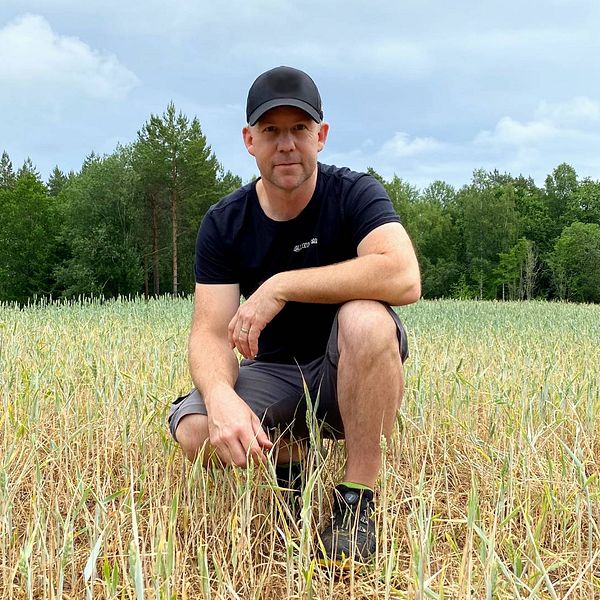 Bilden visar en man i 40-års åldern som sitter på huk på ett torrt odlingsfält.