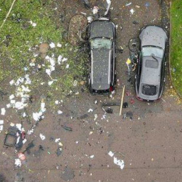 Två bilar står parkerade på en uppfart medan den tredje bilen har blivit till småskrot efter en explosion.
