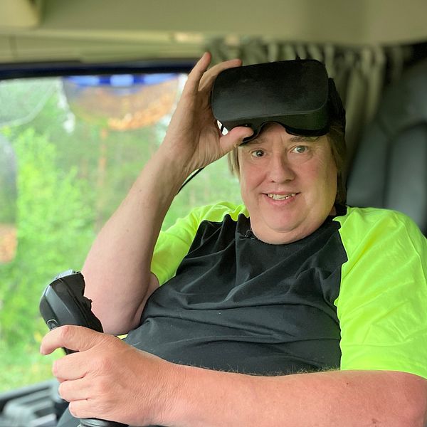 Thomas Bergander, man i svart och neongul t-shirt sitter i en lastbil med en joystick och ett par VR-glasögon i pannan.