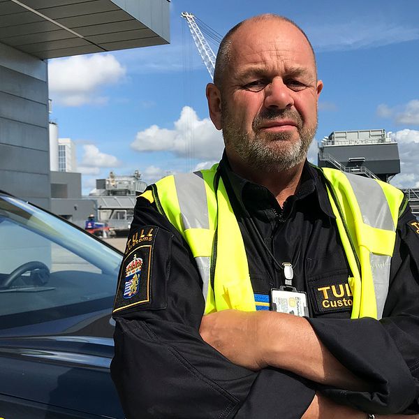 Johan Larsen på Tullverkets kontrollenhet Öst  står i hamnmiljö framför ett tullfordon.